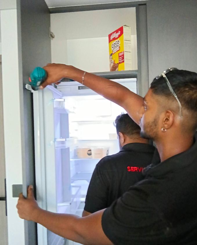 Two technicians repairing a refrigerator door in Ajman